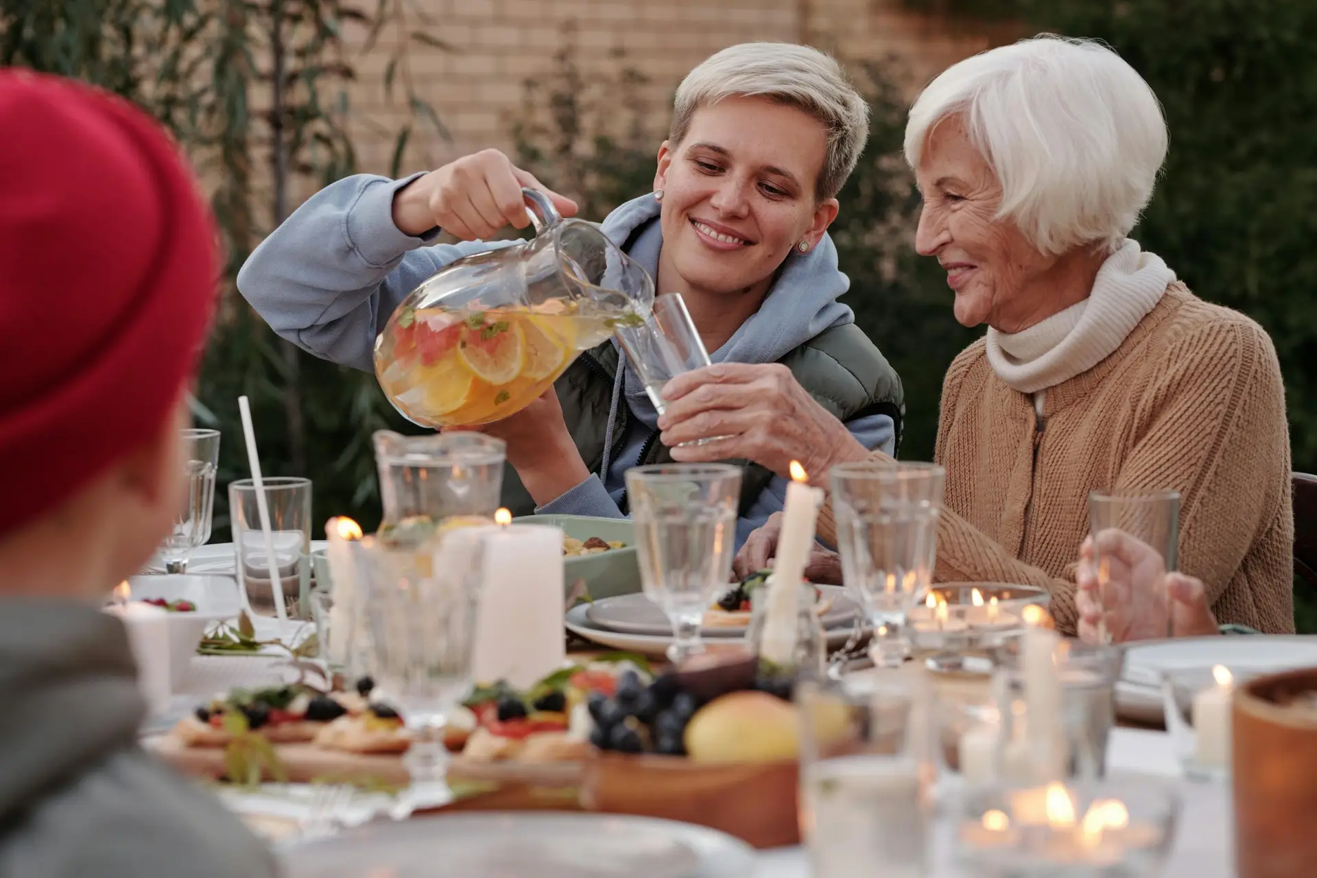 A smiling daughter pours water into her mother’s glass at a cozy family dinner table.
