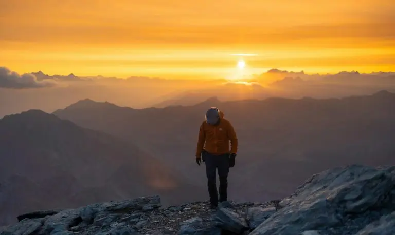 Hiker walking on a mountain peak at sunrise symbolizing financial growth and new opportunities.